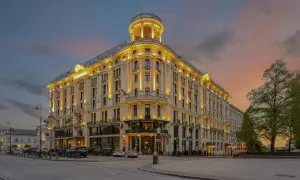 Elegancki budynek Mercure Warszawa Centrum oświetlony wieczorem, z charakterystyczną wieżyczką i ozdobną fasadą, na tle zachodzącego słońca.