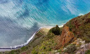 Widok z góry na klif i ocean. Tarasowe pola uprawne schodzą do plaży. Madera kiedy jechać? Wiosna i jesień oferują idealną pogodę.