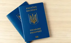 Dwa niebieskie paszporty biometryczne Ukrainy leżą na drewnianym blacie.