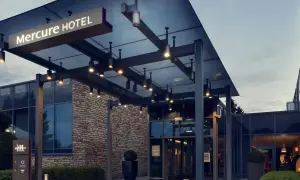 Nowoczesne wejście do hotelu Mercure w Gdańsku, z kamienną fasadą i oświetlonym zadaszeniem.