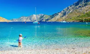Dziecko bawi się na kamienistej plaży w Grecji. Marzysz o tanich lotach z Krakowa gdziekolwiek? To miejsce czeka!