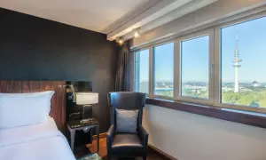 Pokój w Blu Radisson Hamburg z widokiem na wieżę telewizyjną. Wygodne łóżko, fotel i stolik nocny.
