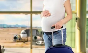 Ciężarna kobieta z walizką na lotnisku, zastanawia się, czy w ciąży można latać samolotem.