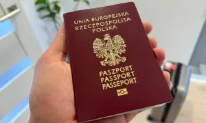 Dłoń trzyma polski paszport z godłem orła.