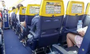 Wnętrze samolotu Boeing 737 Ryanair. Pasażerowie siedzą w rzędach, na oparciach foteli widoczne są instrukcje bezpieczeństwa.
