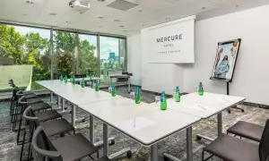 Sala konferencyjna w hotelu Mercure Poznań Centrum gotowa na spotkanie. Stoły ustawione, woda czeka, a za oknem zieleń.