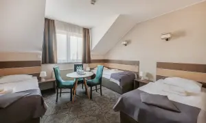 Pokój hotelowy z trzema łóżkami, stolikiem i krzesłami.