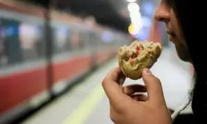 Osoba w kapturze je bułkę na tle pociągu TLK.