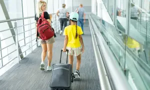 Młoda kobieta z plecakiem i dziewczynka z walizką idą korytarzem lotniska. To może być ich pierwszy wyjazd nieletniego za granicę bez rodziców.