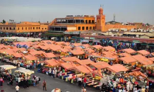 Targowisko w Marrakeszu, gdzie można znaleźć wiele produktów i poznać ceny. W tle budynki i minaret.