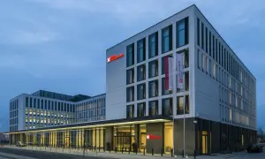 Nowoczesny budynek Hilton Garden Inn Kraków o białej fasadzie z czerwonym logo, z polską flagą przy wejściu.