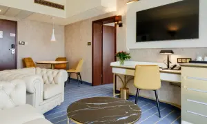 Elegancki pokój w hotelu Diament Wrocław: wygodna sofa, biurko z telefonem i TV, stolik kawowy i okrągły stół z krzesłami.