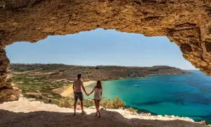 Para zakochanych podziwia widok na turkusowe morze i piaszczystą plażę z jaskini. Malta pogoda w lutym zachwyca słońcem.