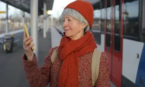 Starsza pani na dworcu sprawdza w telefonie, jak wyrobić kartę seniora PKP.