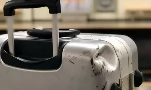 Uszkodzona walizka na lotnisku, z wgnieceniem i zadrapaniami, świadczy o trudach podróży.