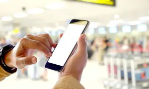 Ręce trzymają smartfon z pustym ekranem. W tle widać zamazany terminal lotniczy, sugerujący, że to idealny moment na **lot odprawa online kiedy** tylko chcesz.