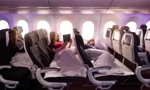 Komfortowy biznes klasa lot. Pasażerowie odpoczywają w wygodnych fotelach, jeden czyta, drugi śpi.
