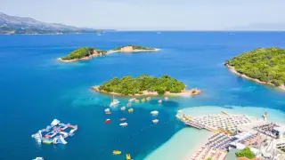 Piękne, turkusowe morze w Albanii, z zielonymi wysepkami i plażą pełną leżaków.
