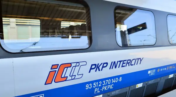 Boczna ściana pociągu PKP Intercity z logo IC. Widoczne okna, w których odbija się niebo i peron. To właśnie eic co to za pociąg!