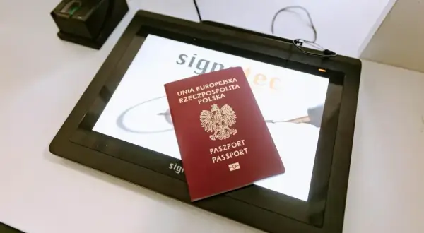Polski paszport leży na ekranie urządzenia do podpisu elektronicznego, obok skanera linii papilarnych. Ważność paszportu jest kluczowa przy podróżach.