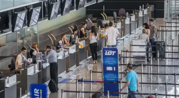 Odprawa online ile wcześniej na lotnisku? Pasażerowie przy stanowiskach LOT i Wizz Air, niektórzy z bagażami, czekają na odprawę.