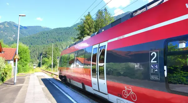Czerwony pociąg na tle górskich krajobrazów. Chcesz wiedzieć, jak kupić bilet na pociąg w Niemczech? To proste, wystarczy podejść do kasy lub automatu.