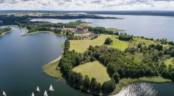 Żaglówki na jeziorze koło pałacu w Krainie Wielkich Jezior Mazurskich. Nietypowe atrakcje Podlasia to także piękne krajobrazy i sporty wodne.