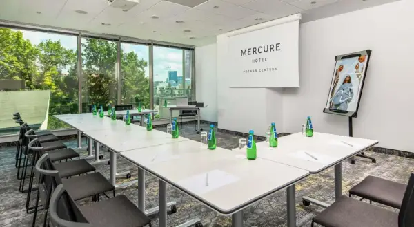 Sala konferencyjna w hotelu Mercure Poznań Centrum gotowa na spotkanie. Stoły ustawione, woda czeka, a za oknem zieleń.