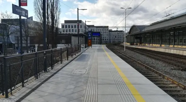 Peron 6 na dworcu Wrocław Główny, z którego odjeżdża pociąg. Nowoczesny peron z żółtym pasem bezpieczeństwa i budynkami w tle.