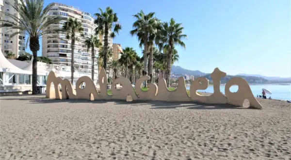 Malaga plaże: piasek, palmy i napis "Malaga" na tle budynków i morza.