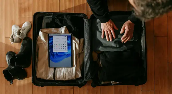 Pakowanie walizki na podróż. Sprawdzam wymiary bagażu rejestrowanego 20 kg Wizzair na tablecie, obok leżą buty i ubrania.
