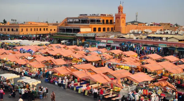 Targowisko w Marrakeszu, gdzie można znaleźć wiele produktów i poznać ceny. W tle budynki i minaret.