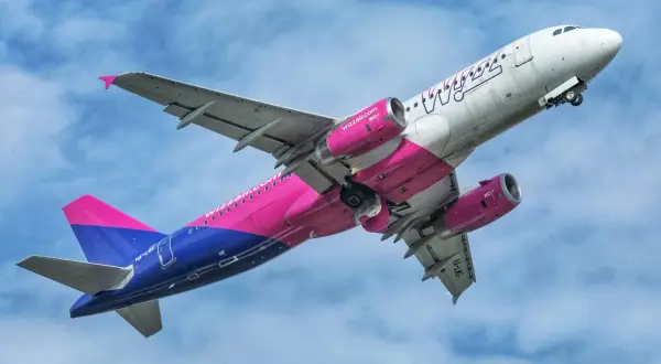 Samolot Wizz Air z różowo-niebieskim ogonem wznosi się na tle błękitnego nieba. Chcesz wiedzieć, jak przełożyć lot w Wizzair?