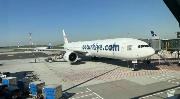 Samolot linii lotniczych MGA z napisem "goturkiye.com" na lotnisku. W tle widać inny samolot i rękaw.