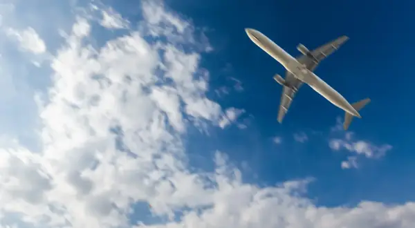 Samolot leci na tle błękitnego nieba z chmurami. Zastanawiasz się, ile się leci do Marsa Alam?