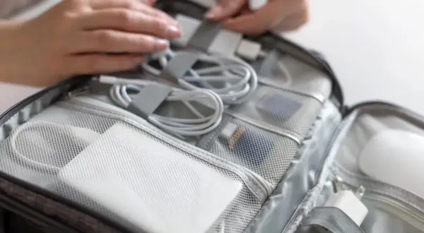 Organizacja akcesoriów elektronicznych w torbie podręcznej: biały powerbank, kable i ładowarki w przegródkach.