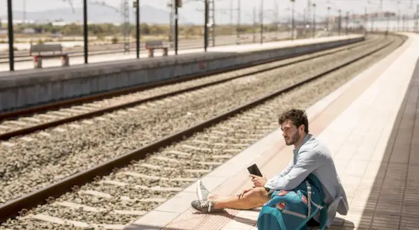 Mężczyzna siedzi na peronie, trzymając telefon. Spóźniłem się na pociąg, co z biletem?