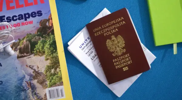 Polski paszport i bilet lotniczy na podróż do Kanady. Obok magazyn podróżniczy i zielony notatnik.
