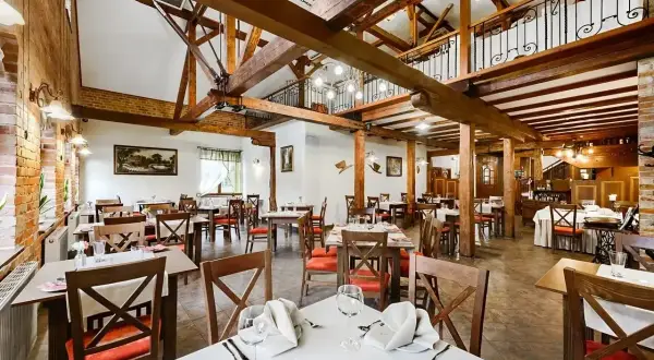 Przytulna restauracja w hotelu Młyn Elbląg. Drewniane belki, ceglane ściany i eleganckie stoły tworzą niepowtarzalny klimat.