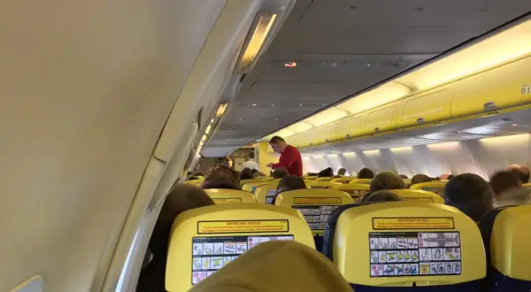 Wnętrze samolotu Ryanair, pasażerowie siedzą w rzędach. Na oparciach siedzeń widoczne są żółte tabliczki z instrukcjami bezpieczeństwa, co może uspokoić osoby zastanawiające się, czy Ryanair jest bezpieczny.