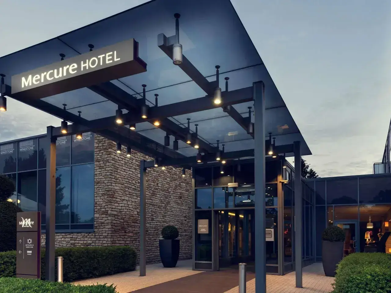 Nowoczesne wejście do hotelu Mercure w Gdańsku, z kamienną fasadą i oświetlonym zadaszeniem.