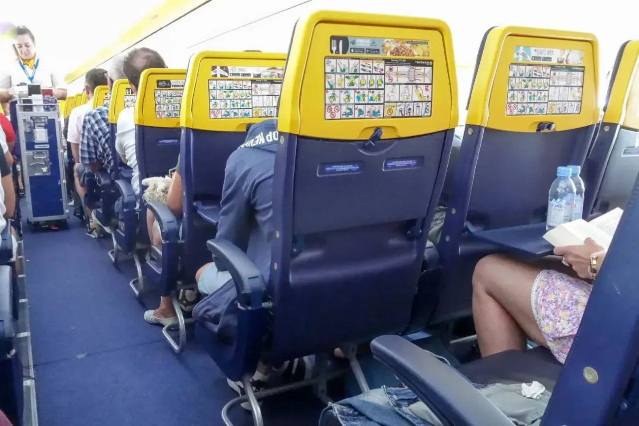 Wnętrze samolotu Boeing 737 Ryanair. Pasażerowie siedzą w rzędach, na oparciach foteli widoczne są instrukcje bezpieczeństwa.