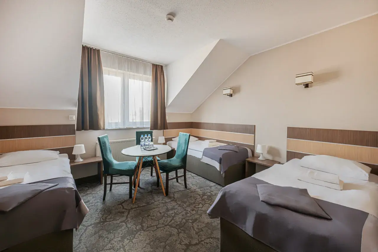 Pokój hotelowy z trzema łóżkami, stolikiem i krzesłami.