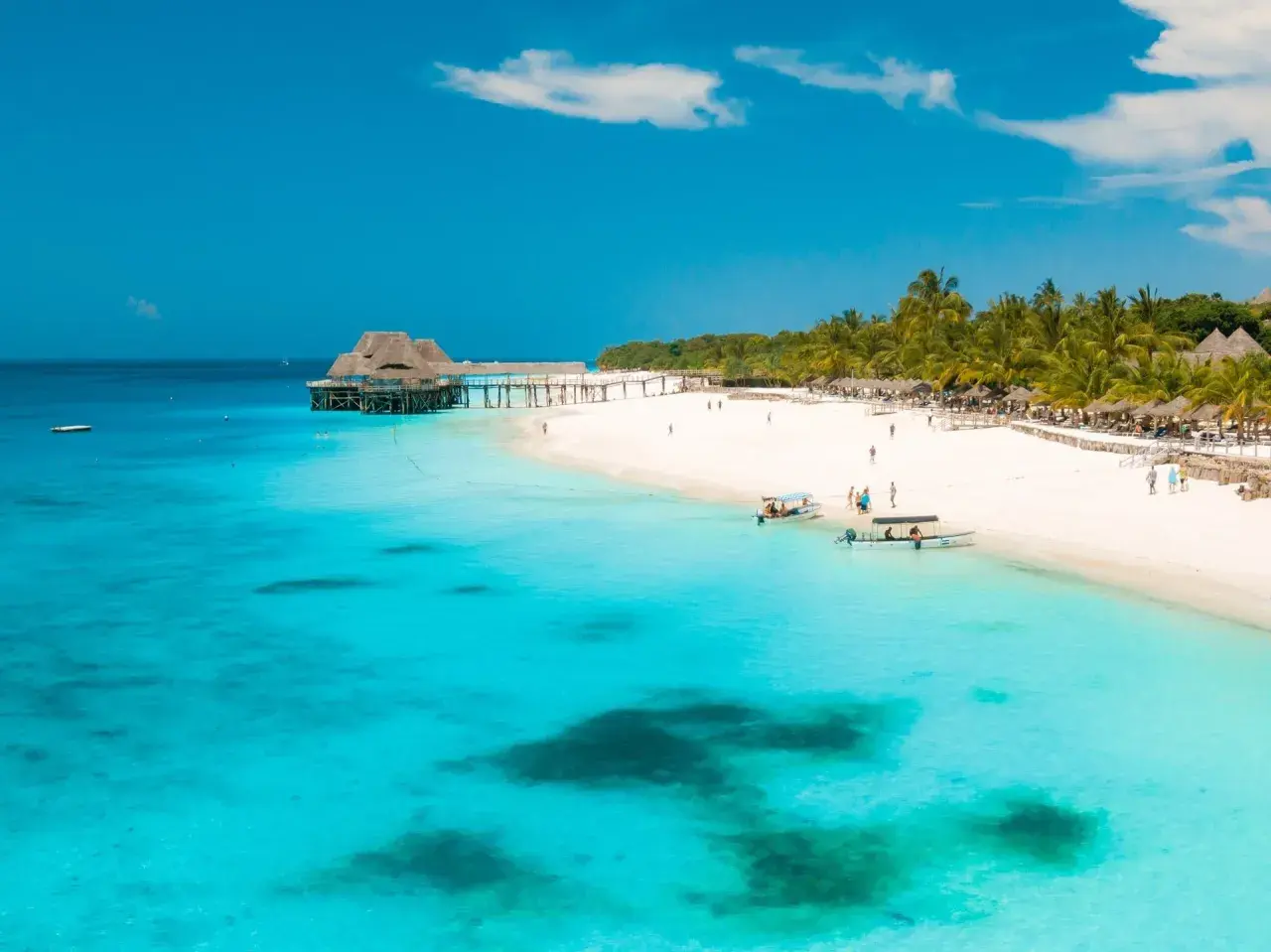 Rajskie zanzibar wakacje: biała plaża, palmy, turkusowa woda i drewniany pomost z domkami na wodzie. Idealne miejsce na relaks.