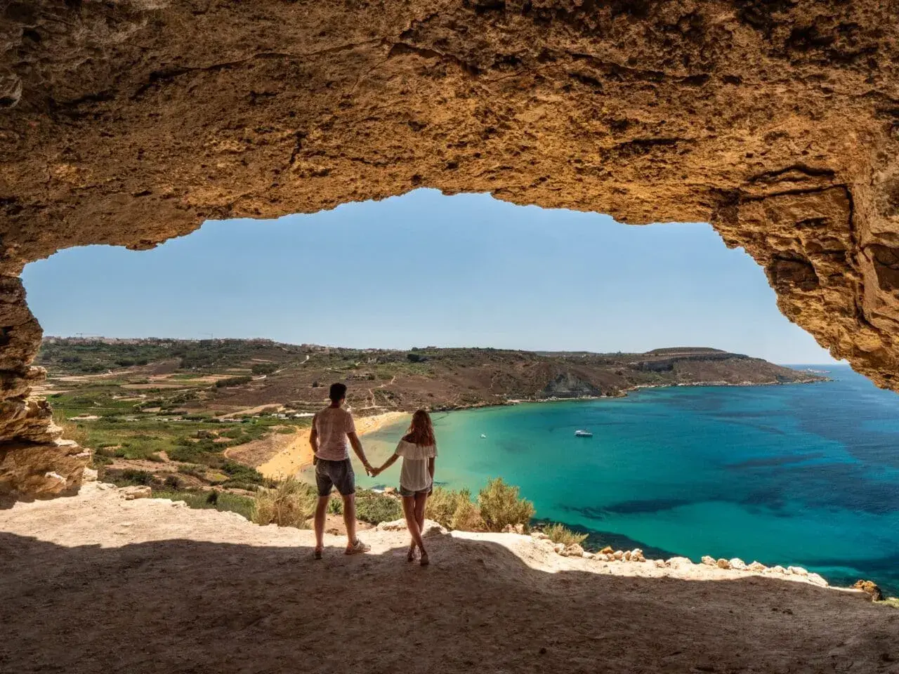 Para zakochanych podziwia widok na turkusowe morze i piaszczystą plażę z jaskini. Malta pogoda w lutym zachwyca słońcem.