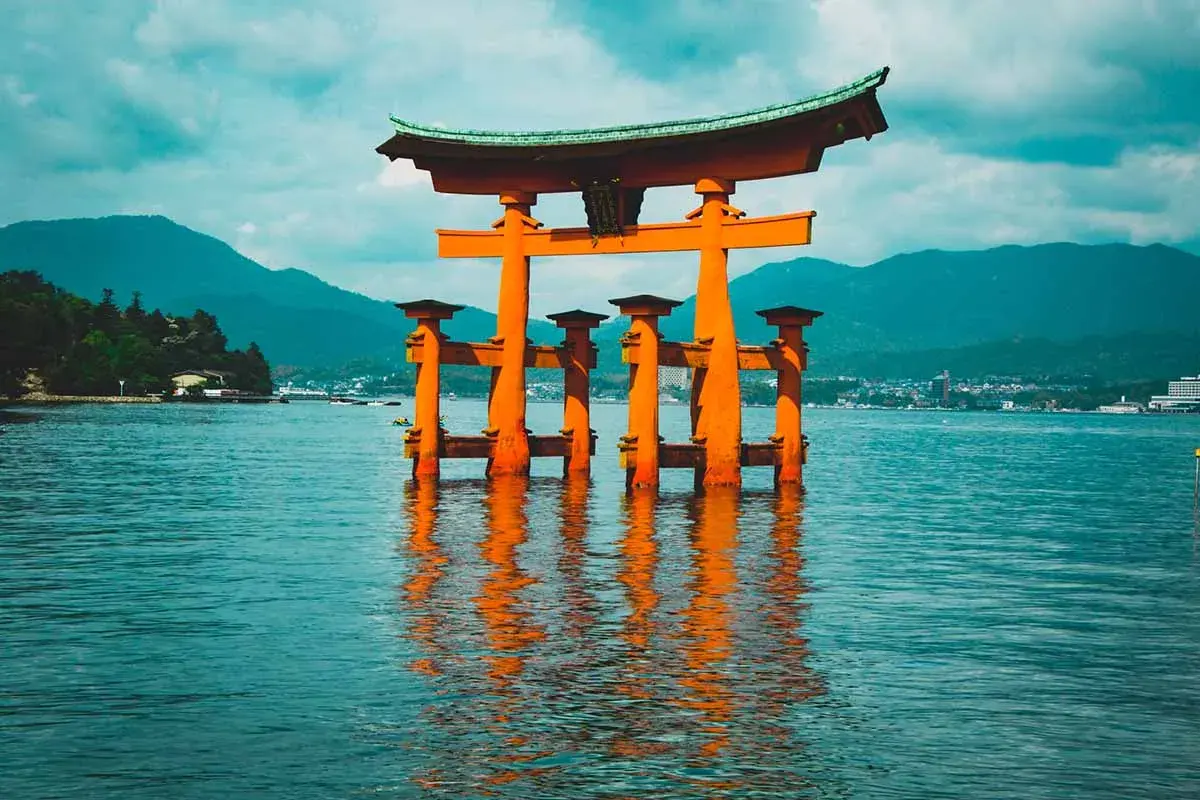Pomarańczowa brama torii w wodzie, idealne miejsce na Japonia wycieczka. W tle góry i miasto.