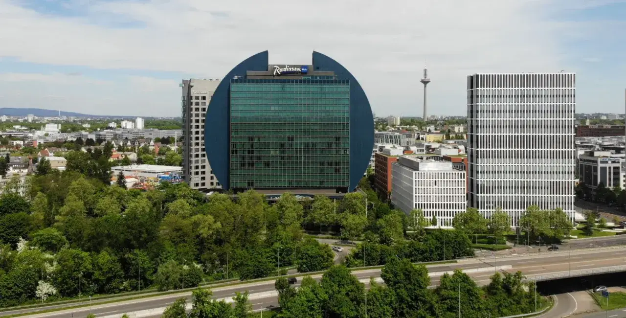 Charakterystyczny budynek Radisson Blu we Frankfurcie, otoczony zielenią i nowoczesną architekturą.