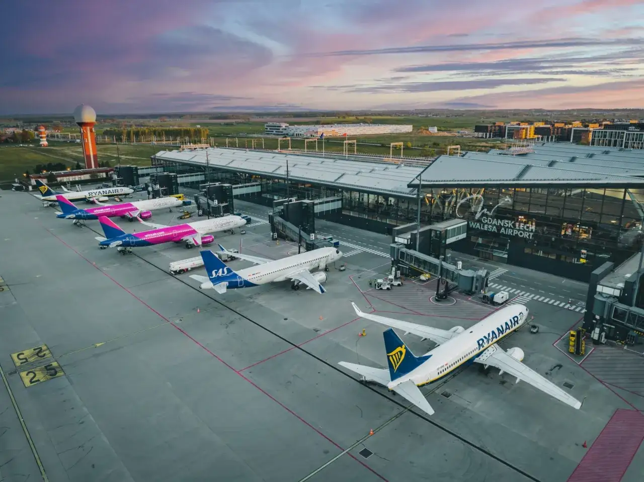 Samoloty Ryanair, Wizz Air i SAS czekają na pasażerów na płycie lotniska. W tle nowoczesny terminal i zachodzące słońce, idealne na loty krajowe.