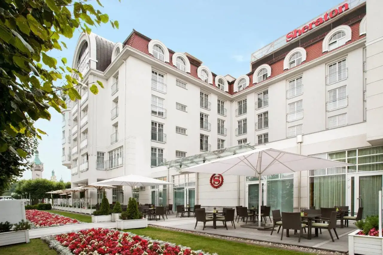 Elegancki hotel Sheraton Sopot z białym murem, czerwonym dachem i tarasem z parasolami.