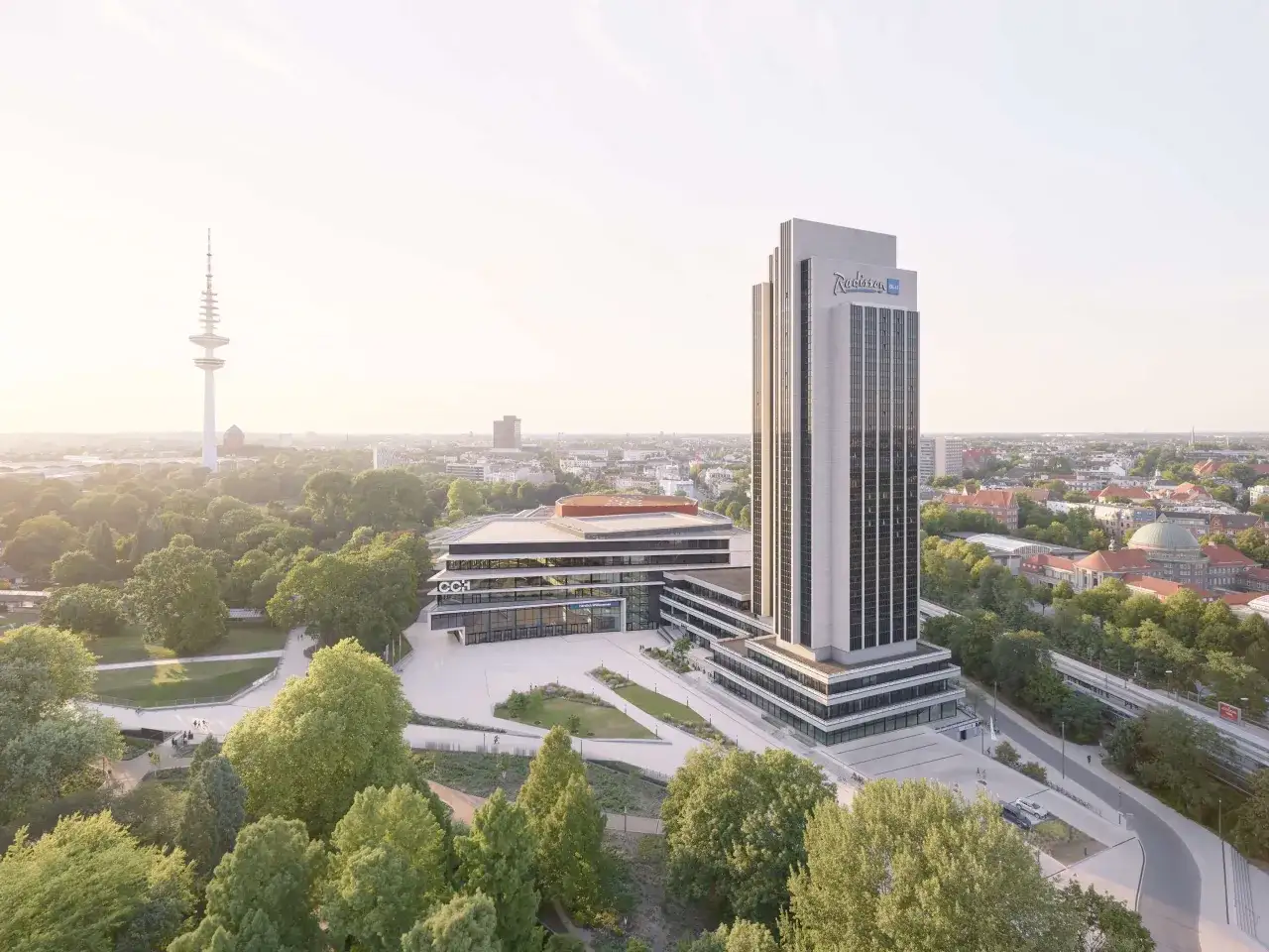 Radisson Blu Hotel w Hamburgu, z charakterystycznym wieżowcem i nowoczesnym budynkiem konferencyjnym, otoczony zielenią.